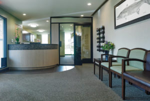 The reception area is generously sized and professional. The chairs and wall colors are in shades of green, blending harmoniously with the lush landscape outside. Glass walls and doors provide privacy while maintaining an open feel in the office.